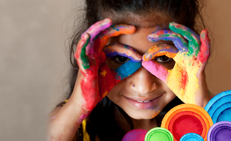 child finger painting while holding fingers to her face