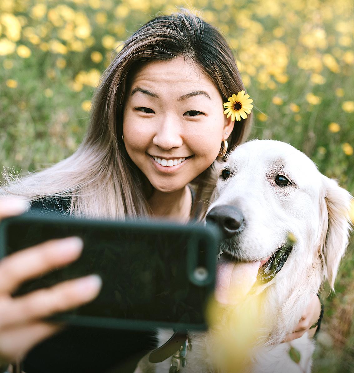 woman taking a photo with a golden retriever in a field